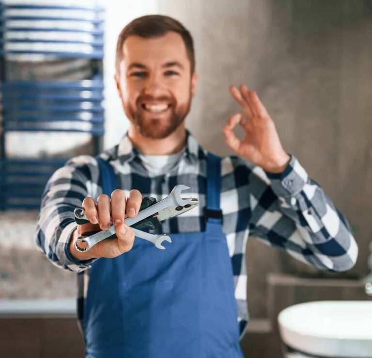 Holding wrenches. Plumber in blue uniform is at work in the bathroom