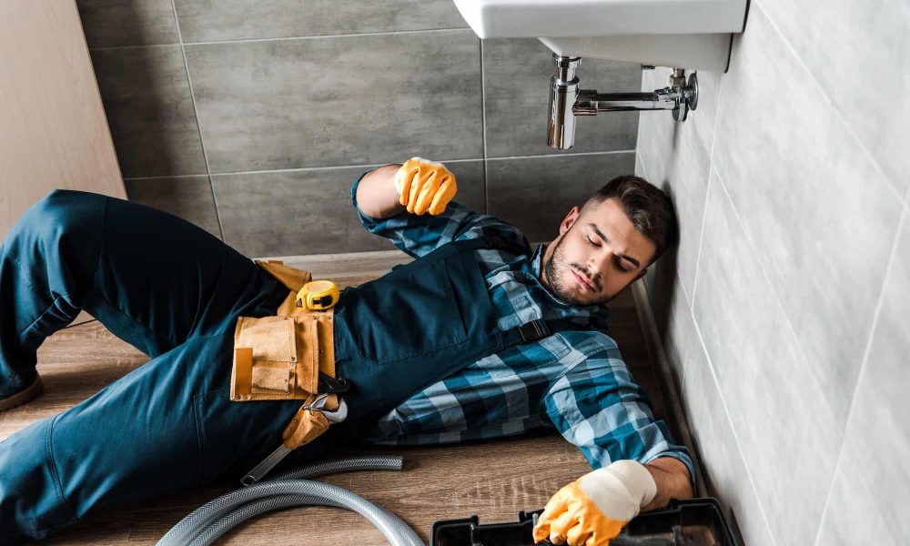 bearded handyman lying on floor near toolbox in bathroom